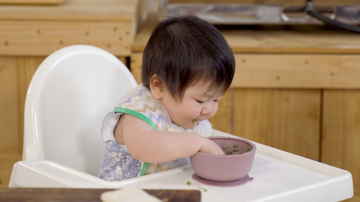 https://www.wonderbaby.org/wp-content/uploads/2022/05/Baby-sitting-on-a-chair-at-home-is-grabbing-food-inside-the-bowl.jpg
