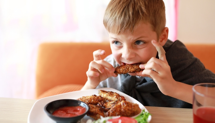 Child eating roasted chicken wings in restaurant.