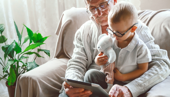 An elderly grandfather and his little grandson are using a tablet device together,.