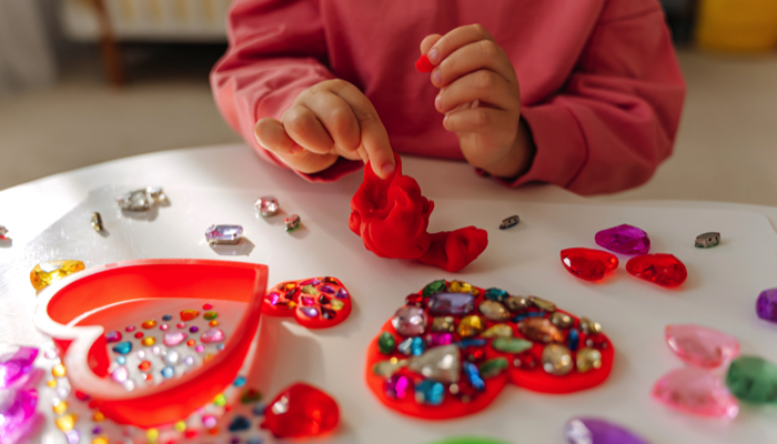 A little girl creating tactile art with beads and clay.