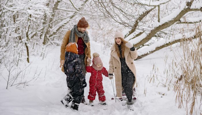 A Family in Winter Clothes Walking on a Snow-Covered Ground near the Tree Branches