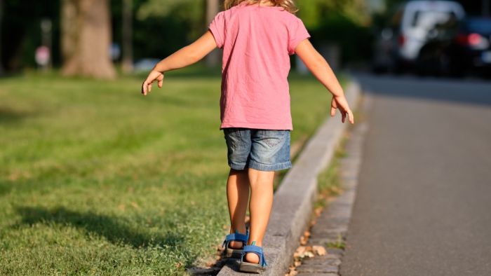 Child maintains equilibrium while walking in a heel-to-toe manner on the edge of a sidewalk