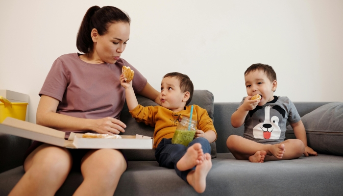 Mother and Sons Eating Snack while Sitting on a Couch