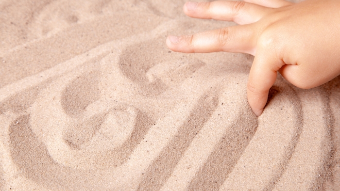 Child drawing a pattern picture in the sand with their finger