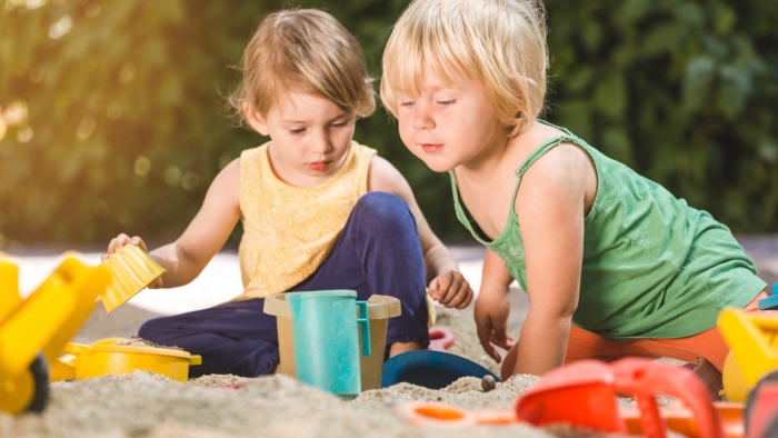 Two children playing in a sandpit with various sand toys