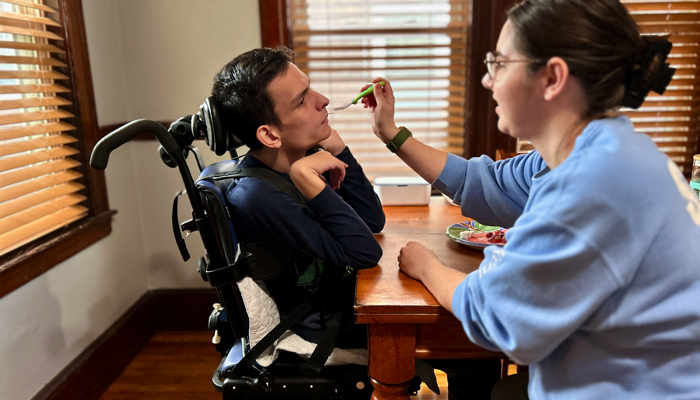 Ivan sitting in his adaptive chair at the table eating a meal.