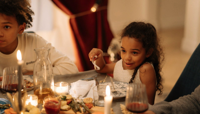 Two kids at the table eating a Thanksgiving meal with family.